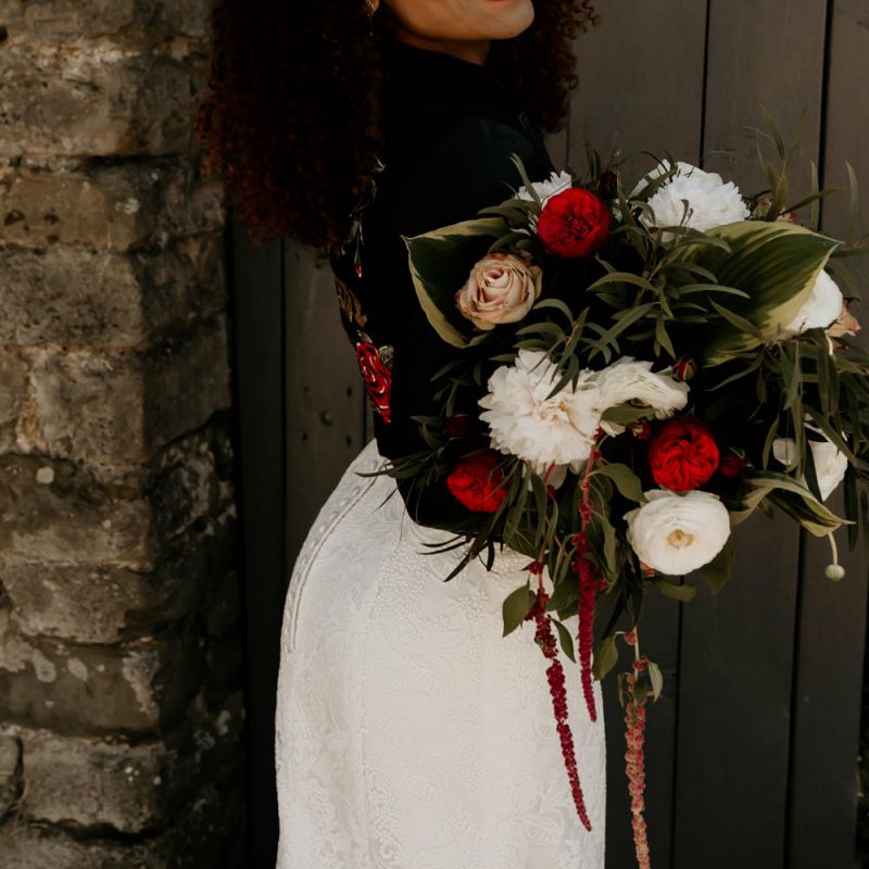 Black Bride with Afro Hair Wearing Leather Jacket Holding a Red, White and Foliage Bouquet