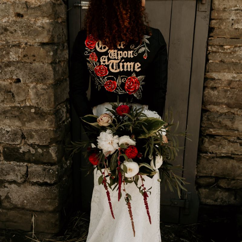 Black Bride with Afro Hair Wearing Leather Jacket Holding a Red, White and Foliage Bouquet