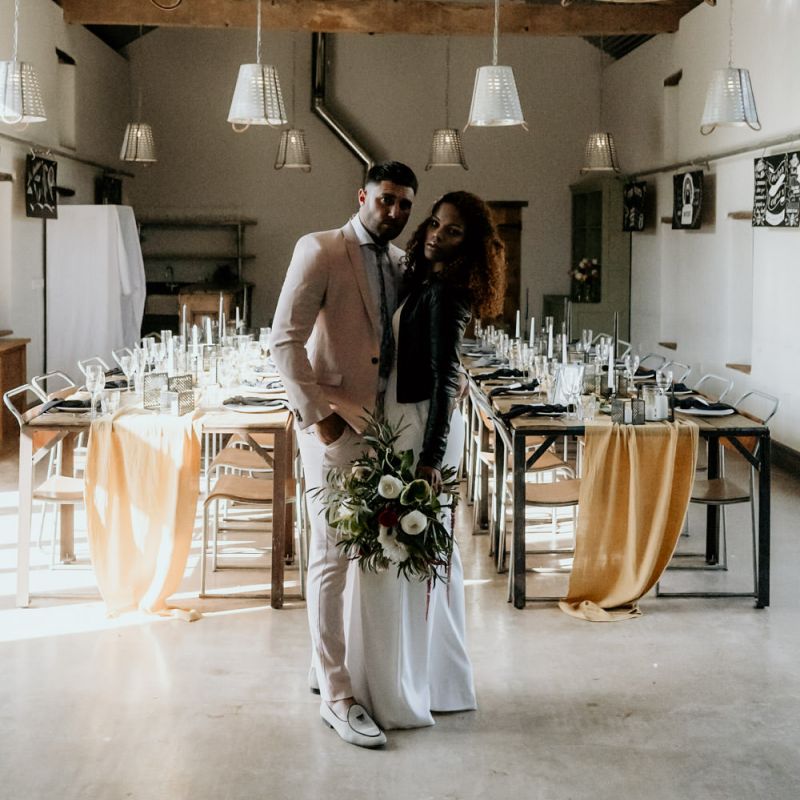 Black Bride in Lace Wedding Dress and Leather Jacket Standing Next to Groom in Blazer and Loafers
