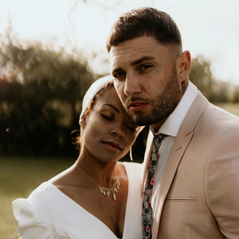 Black Bride in White Jumpsuit with Head Wrap  and Groom in Pink Blazer