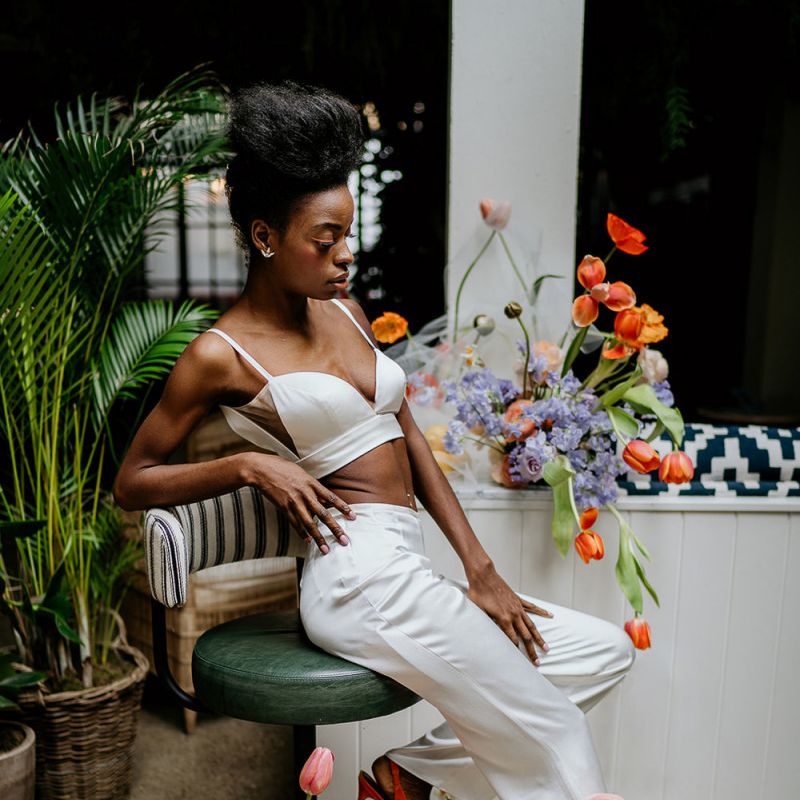 Black bride in trouser outfit surrounded by colourful spring wedding flowers