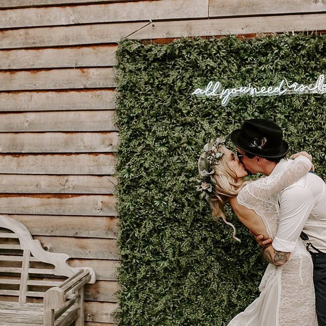bride and groom kiss in front of foliage backdrop and neon sign