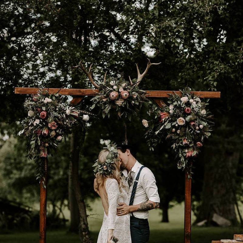 Bride clutches Protea bouquet as she kisses groom under wooden arch decorated in flowers