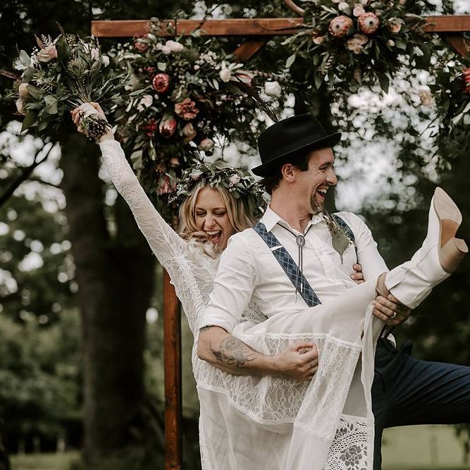 Groom plays guitar on brides leg who clutches Protea bouquet and wears bridal boots