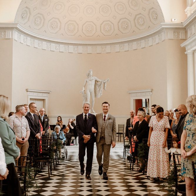 Groom in beige checked suit walking down the aisle with his father