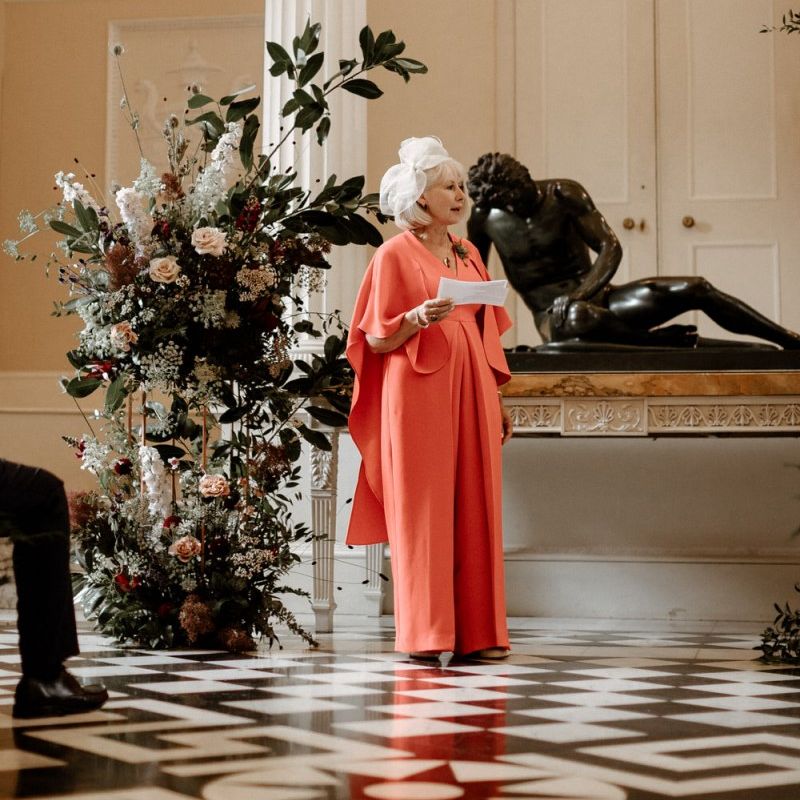 Mother of the groom in coral outfit performing a wedding reading