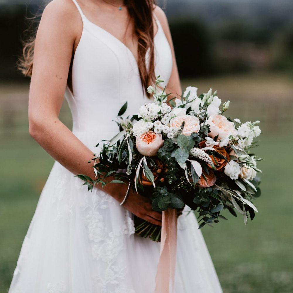 Bride holding a romantic peach and white flower bouquet with foliage and ribbon