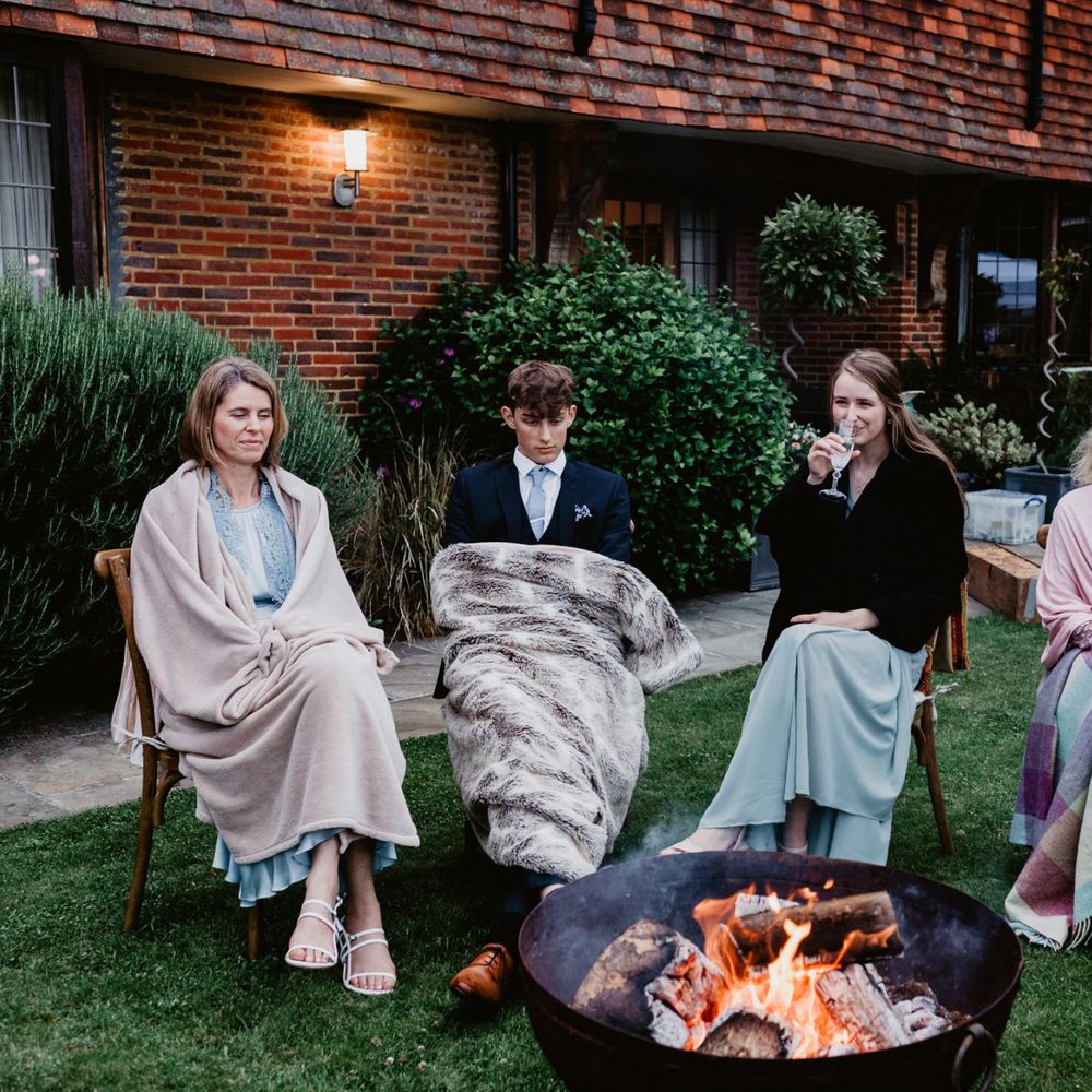 Wedding guests wrapped in blankets sat by the firepit