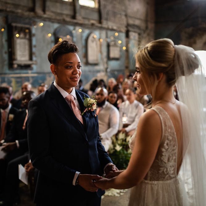 Bride in Navy Suit and Pink Tie and Bride in Romantic Flora Mila Wedding Dress Holding Hands at the Altar