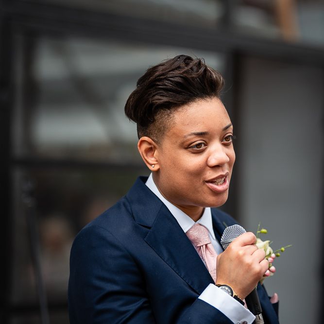 Bride in Navy Wedding Suit with Pink Tie Delivering Her Wedding Speech