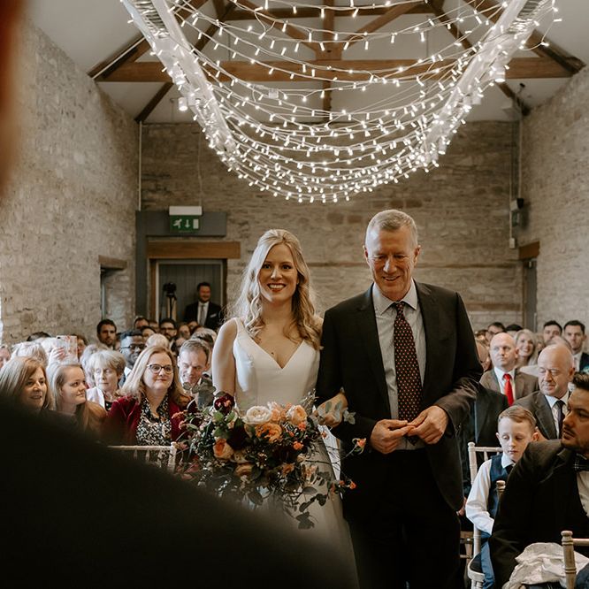 Bride walks down the aisle under fairy light canopy