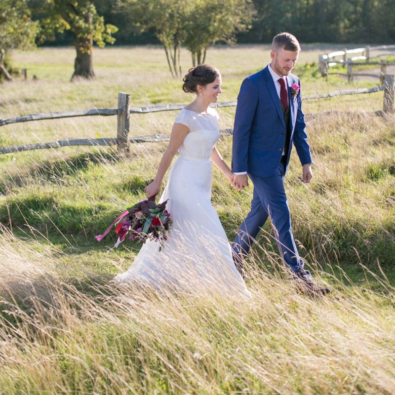 Bride in Jesus Peiro Wedding Dress and Groom in Blue  Hugo Boss Suit Walking Through  the Countryside