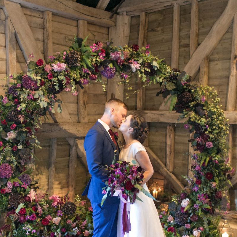 Bride in Jesus Peiro Wedding Dress and Groom in Blue  Hugo Boss Suit Standing in Front of a Floral Moon Gate
