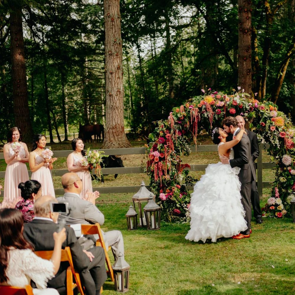 Bride and groom kissing in front of the flower arch at outdoor wedding ceremony