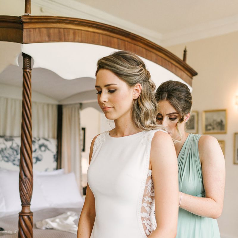 Bridesmaid Helping the Bride into Her Fitted Pronovias Wedding Dress with Lace Side Panels