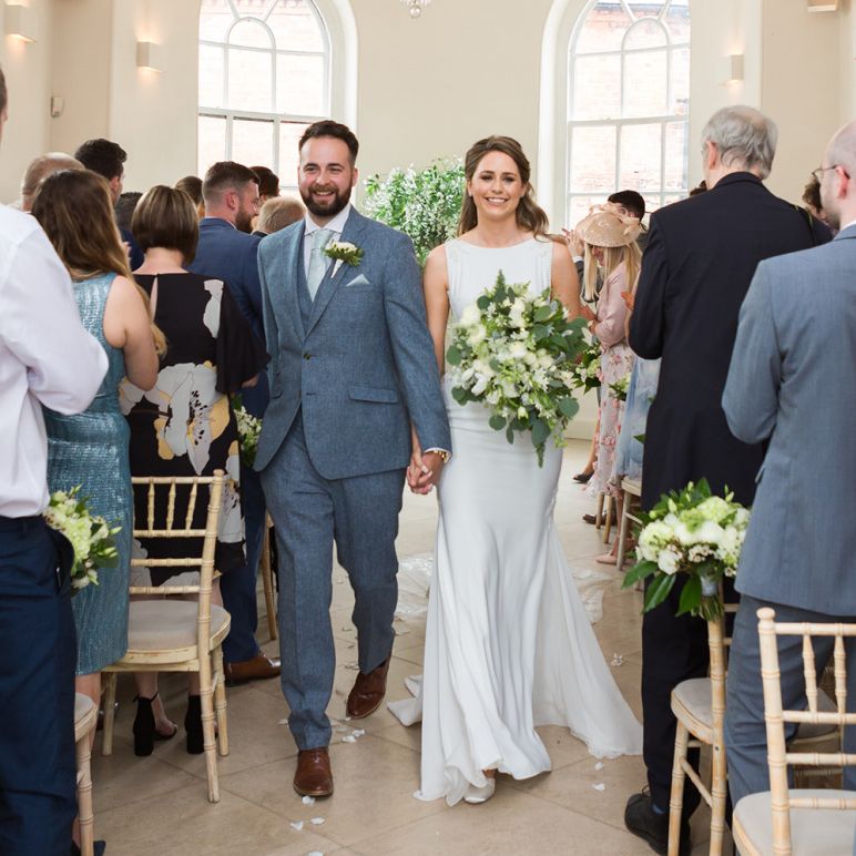 Bride in Pronovias Wedding Dress and Groom in Grey Suit Walking Up The Aisle as Husband and Wife