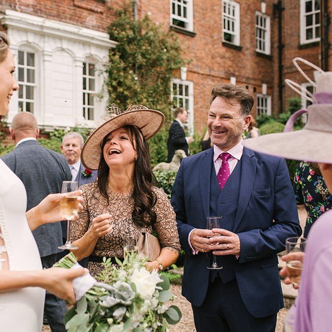 Bride in Pronovias Wedding Dress with Lace Side Panels Enjoying a Glass of Champagne with Wedding Guests