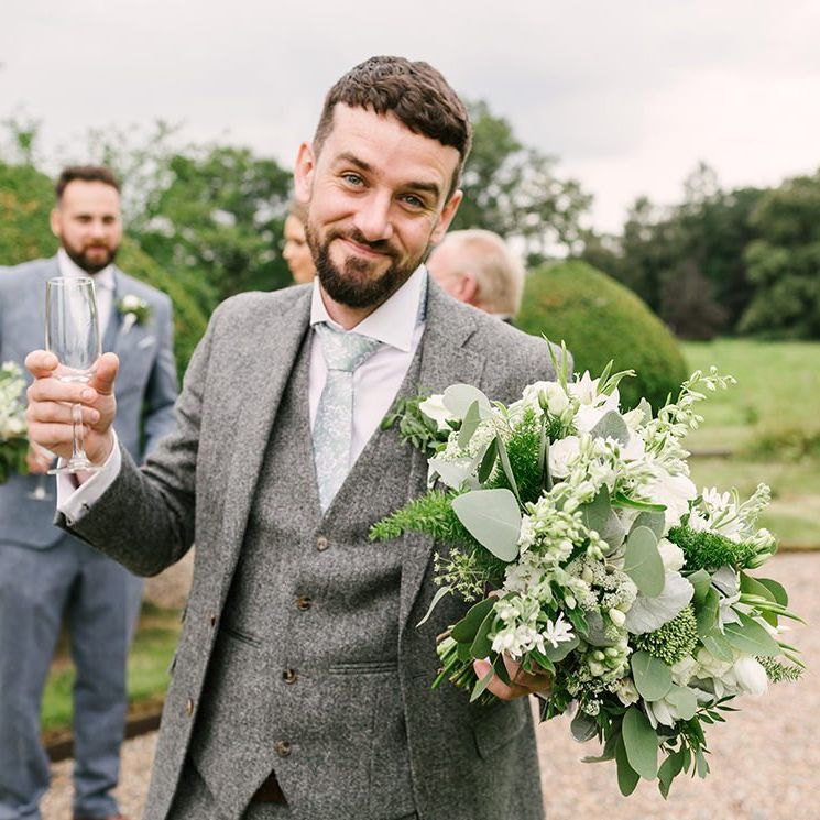 Groomsman in Grey Wedding Suit Holding a White and Green Wedding Bouquet
