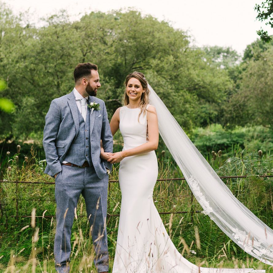 Bride in Fitted Pronovias Wedding Dress Holding Her Grooms Arm  in a Light Grey Wedding Suit