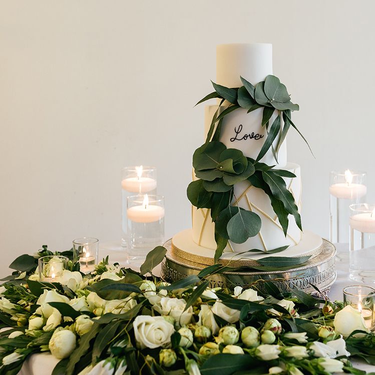 White Wedding Cake Surrounded by Foliage and Candles