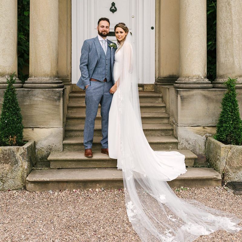 Bride in Pronovias Wedding Dress and Cathedral Length Veil and Groom in Grey Wedding Suit