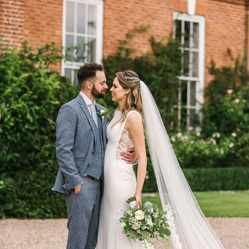 Bride in Pronovias Wedding Dress with Lace Side Inserts and Groom in Light Grey Wedding Suit