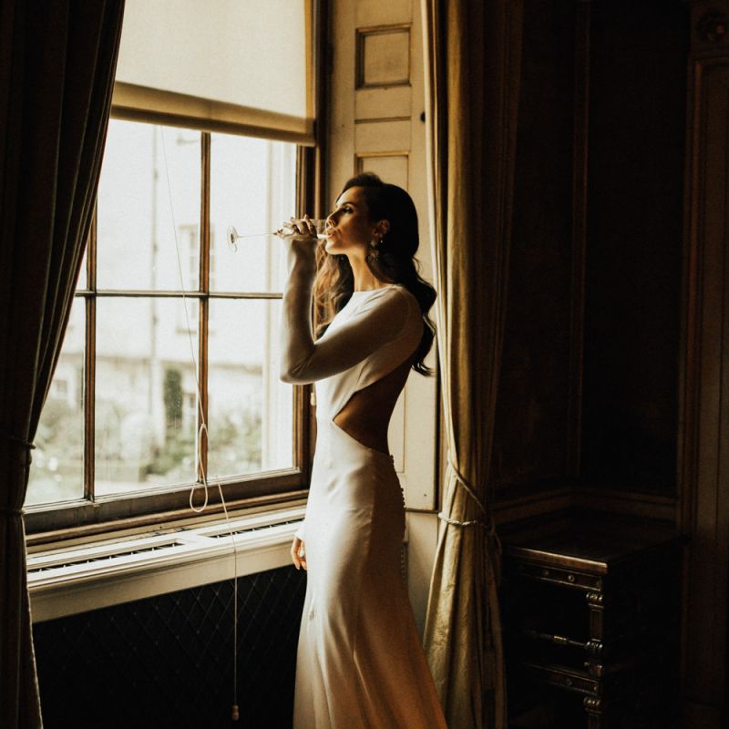 Beautiful Bride Standing at The Window  Sipping Champagne