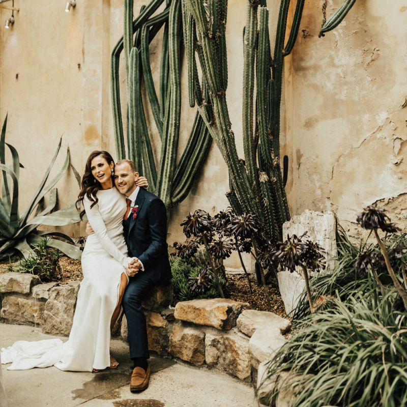 Bride Sitting on Her Grooms Knee with Tropical Plants Backdrop