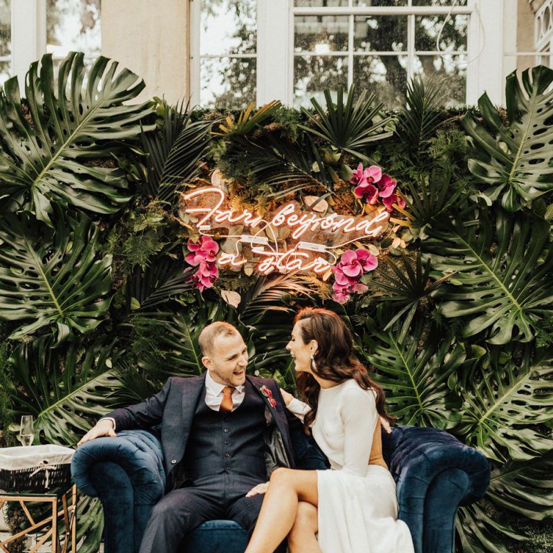Bride and Groom Sitting on a Love Seat with Neon Sign Wedding Sign