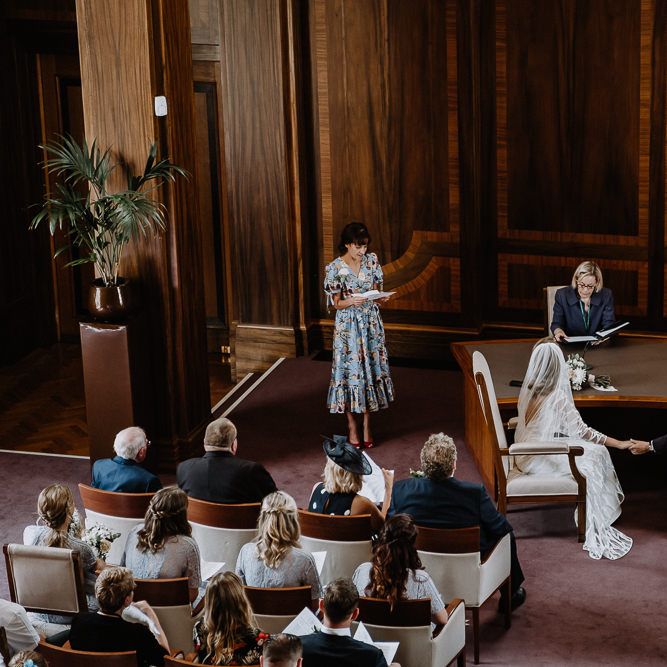 Bride in Embroidered Tulle Halfpenny London Dress with High Neckline, Batwing Sleeves and Low V Back | Fingertip Length Veil from Florence &amp; Dot | Bridal Bouquet of White and Blush Pink Flowers with Eucalyptus and Trailing Silk Ribbon | Groom in Navy Slim Fit Suit with Checked Double Breasted Waistcoat and Blush Pink Knitted Tie | Wedding Ceremony at Stoke Newington Town Hall | Floral Arch and Bride in Batwing Sleeve Halfpenny Dress for London Pub Wedding | Caitlin + Jones