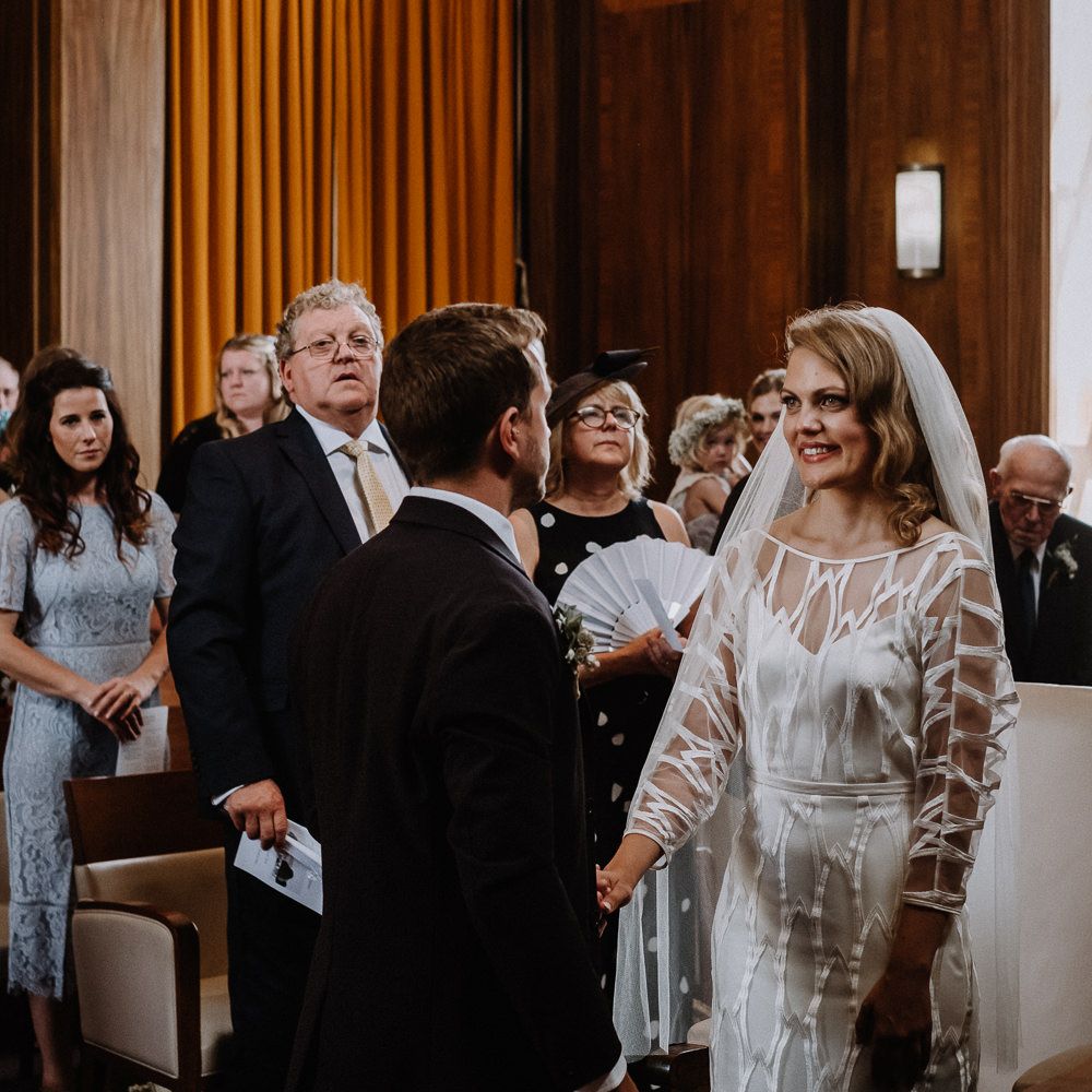 Bride in Embroidered Tulle Halfpenny London Dress with High Neckline, Batwing Sleeves and Low V Back | Fingertip Length Veil from Florence &amp; Dot | Groom in Navy Slim Fit Suit with Checked Double Breasted Waistcoat and Blush Pink Knitted Tie | Wedding Ceremony at Stoke Newington Town Hall | Floral Arch and Bride in Batwing Sleeve Halfpenny Dress for London Pub Wedding | Caitlin + Jones
