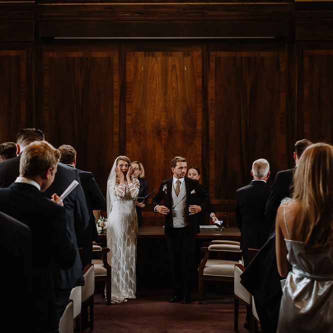 Bride in Embroidered Tulle Halfpenny London Dress with High Neckline, Batwing Sleeves and Low V Back | Fingertip Length Veil from Florence &amp; Dot | Groom in Navy Slim Fit Suit with Checked Double Breasted Waistcoat and Blush Pink Knitted Tie | Wedding Ceremony at Stoke Newington Town Hall | Floral Arch and Bride in Batwing Sleeve Halfpenny Dress for London Pub Wedding | Caitlin + Jones