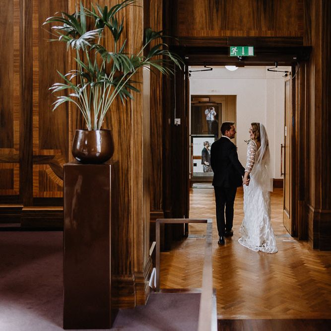 Bride in Embroidered Tulle Halfpenny London Dress with High Neckline, Batwing Sleeves and Low V Back | Fingertip Length Veil from Florence &amp; Dot | Groom in Navy Slim Fit Suit with Checked Double Breasted Waistcoat and Blush Pink Knitted Tie | Wedding Ceremony at Stoke Newington Town Hall | Floral Arch and Bride in Batwing Sleeve Halfpenny Dress for London Pub Wedding | Caitlin + Jones