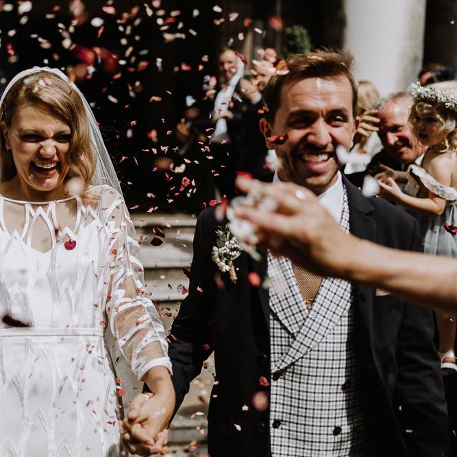 Bride in Embroidered Tulle Halfpenny London Dress with High Neckline, Batwing Sleeves and Low V Back | Fingertip Length Veil from Florence &amp; Dot | Groom in Navy Slim Fit Suit with Checked Double Breasted Waistcoat and Blush Pink Knitted Tie | Confetti Moment at Stoke Newington Town Hall | Floral Arch and Bride in Batwing Sleeve Halfpenny Dress for London Pub Wedding | Caitlin + Jones