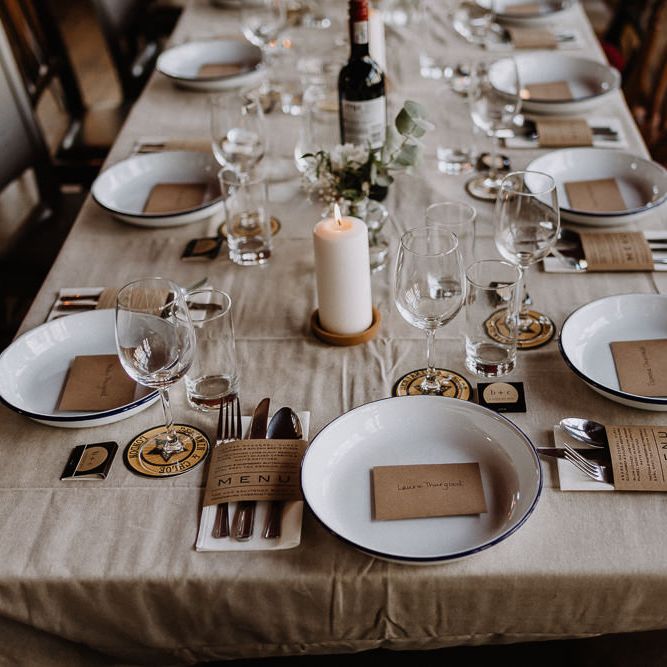 Kraft Paper Wedding Breakfast Menus | White Enamel Plates with Blue Rim | White Pillar Candle | Bud Vase with White Flowers and Eucalyptus | Banquet Table | Mismatched Chairs | Floral Arch and Bride in Batwing Sleeve Halfpenny Dress for London Pub Wedding | Caitlin + Jones