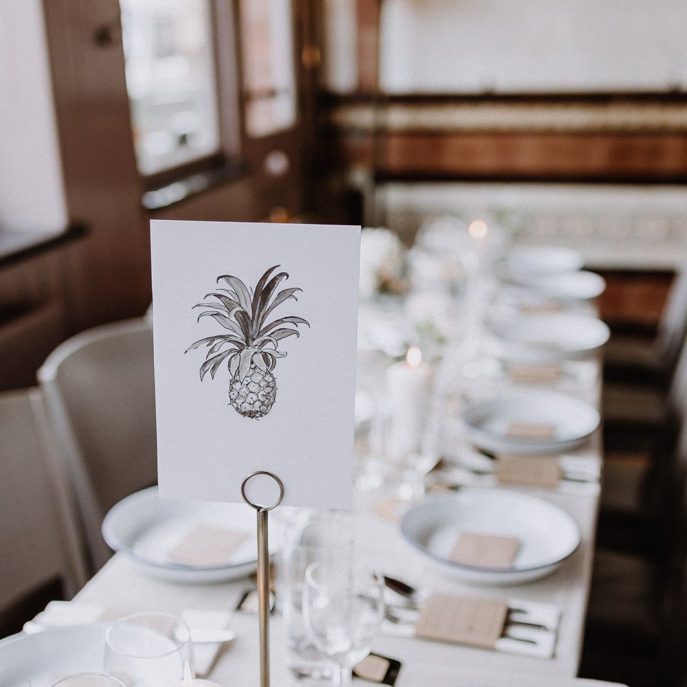 Hand Drawn Table Sign | White Enamel Plates with Blue Rim | White Pillar Candles | Kraft Paper Wedding Breakfast Menus | Banquet Table | Floral Arch and Bride in Batwing Sleeve Halfpenny Dress for London Pub Wedding | Caitlin + Jones