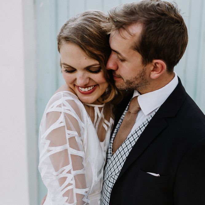 Bride in Embroidered Tulle Halfpenny London Dress with High Neckline, Batwing Sleeves and Low V Back | Groom in Navy Slim Fit Suit with Checked Double Breasted Waistcoat and Blush Pink Knitted Tie | Floral Arch and Bride in Batwing Sleeve Halfpenny Dress for London Pub Wedding | Caitlin + Jones