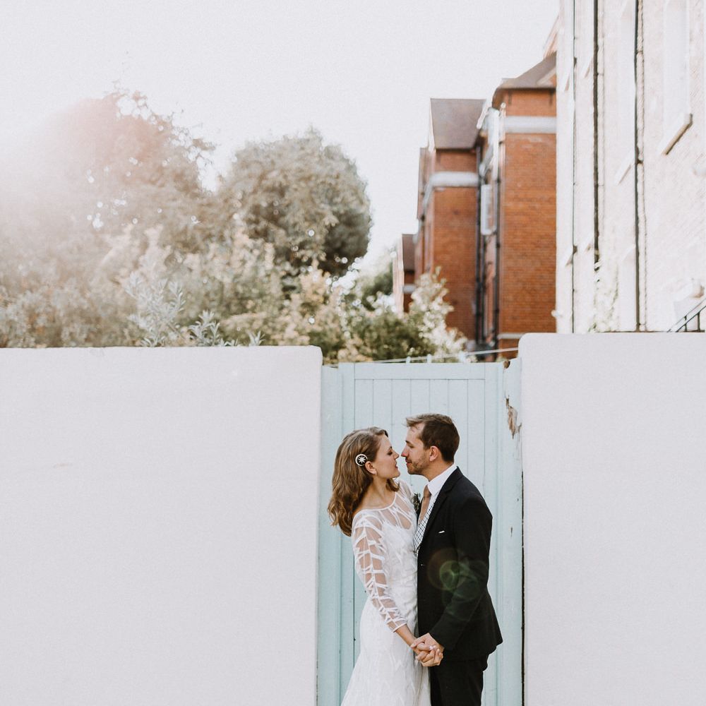 Bride in Embroidered Tulle Halfpenny London Dress with High Neckline, Batwing Sleeves and Low V Back | Anthropologie Hairpiece | Groom in Navy Slim Fit Suit with Checked Double Breasted Waistcoat and Blush Pink Knitted Tie | Floral Arch and Bride in Batwing Sleeve Halfpenny Dress for London Pub Wedding | Caitlin + Jones