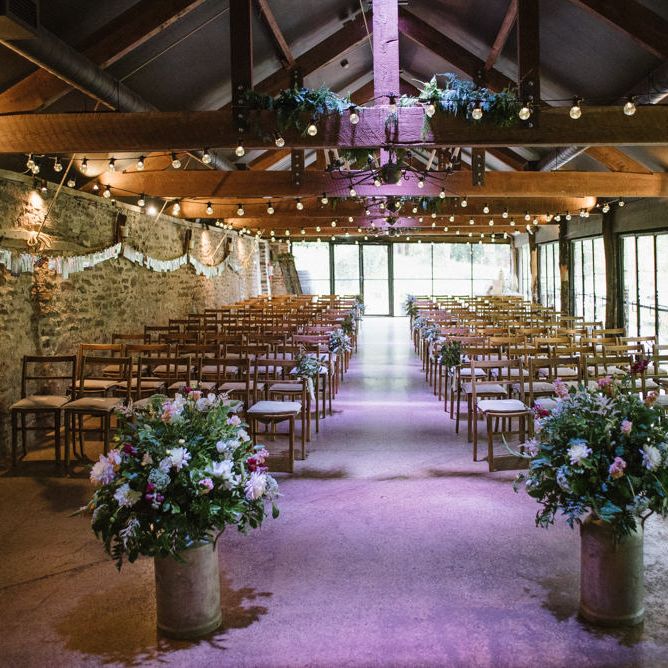 Barn Wedding Ceremony Venue with Two Milk Churns at the Altar Filled with Flowers