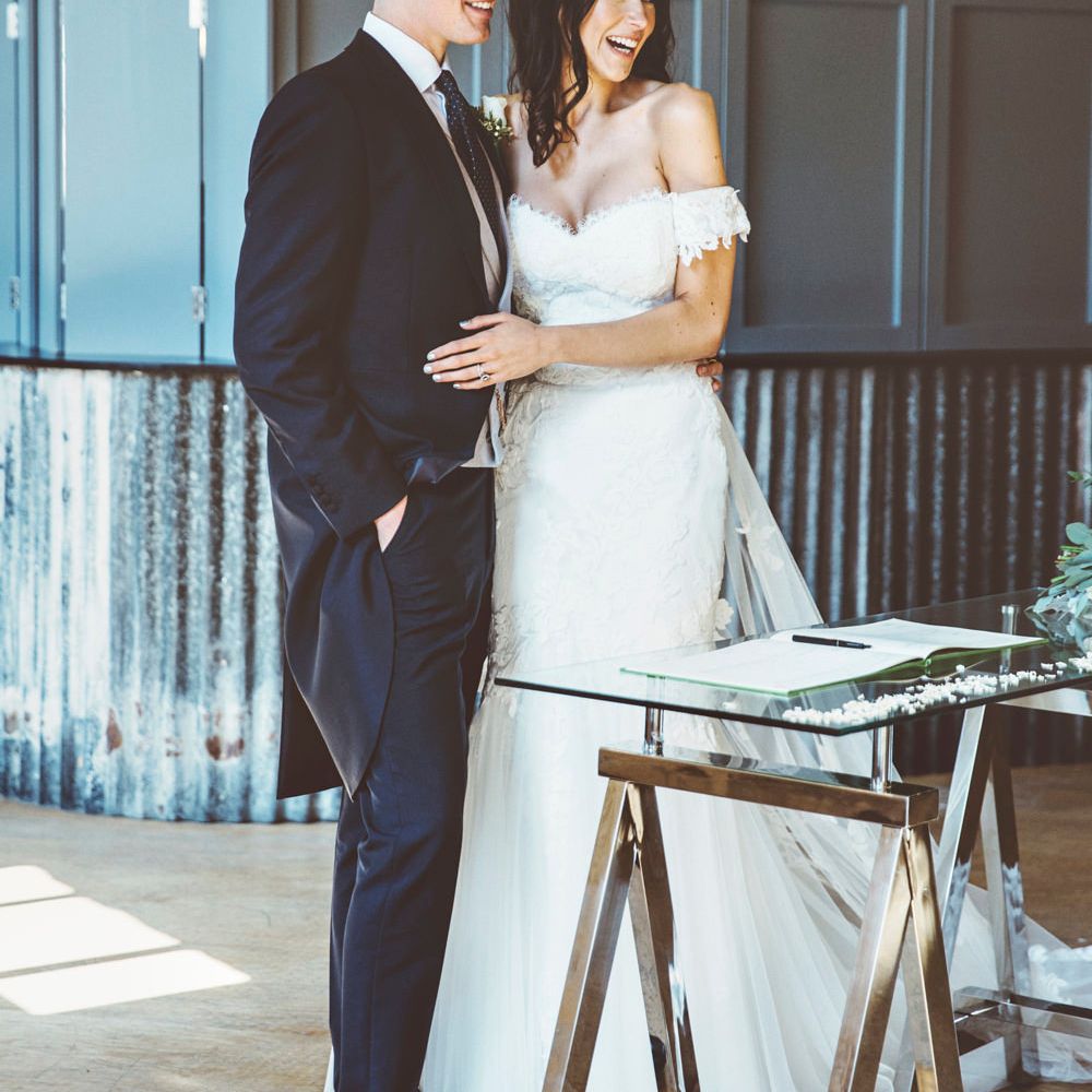 Signing of Register | Bride in Fishtail Pronovias Wedding Dress with Off Shoulder Sleeves and Veil Cape | Groom in Navy Tails and Grey Waistcoat | Bride Wearing Hair Down | Lace Bridal Cape Veil &amp; Fishtail Wedding Dress by Pronovias | On Love and Photography