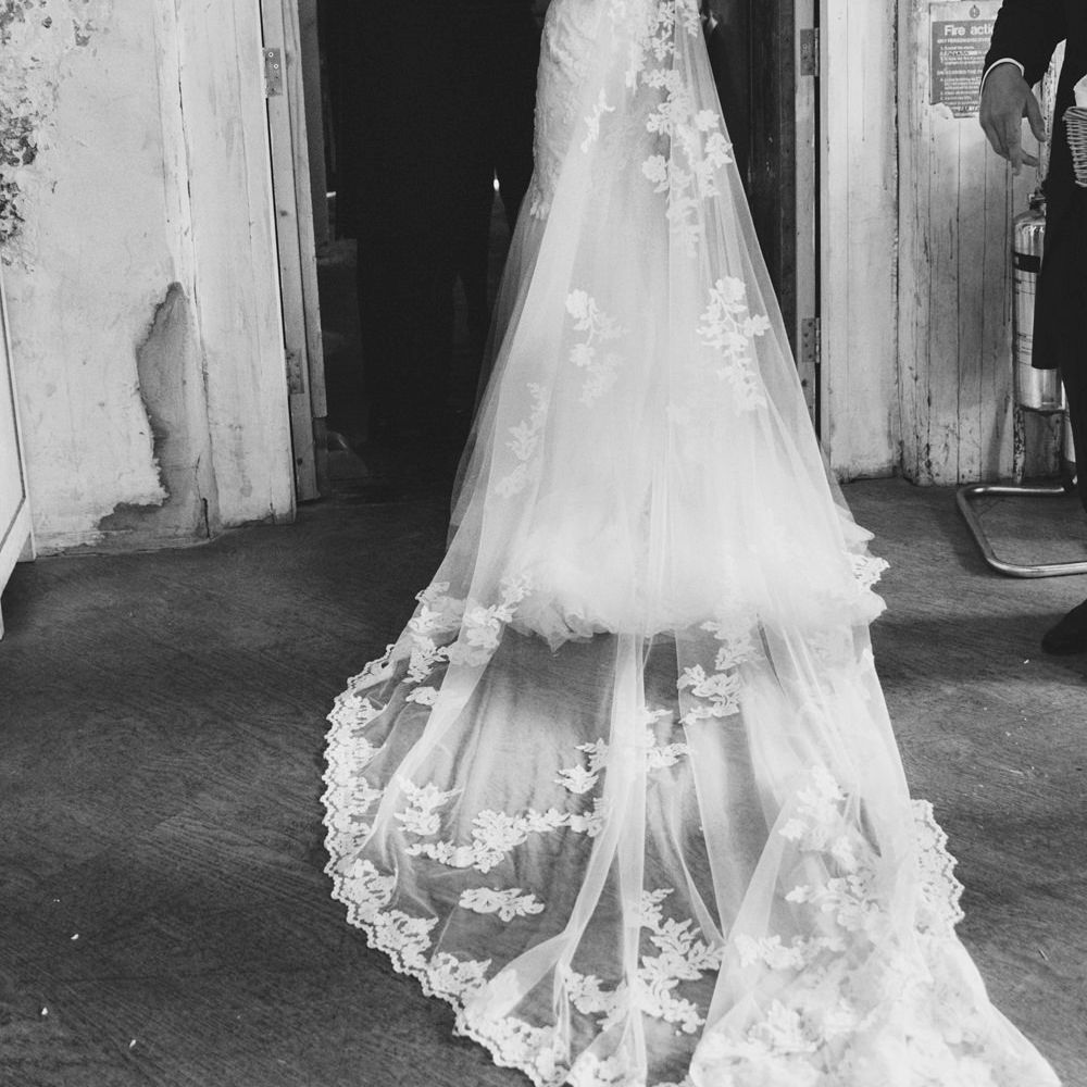 Bride in Embroidered Pronovias Wedding Dress with Off Shoulder Sleeves and Veil Cape | Groom in Navy Tails and Grey Waistcoat | Bride Wearing Hair Down | Bridal Bouquet of White Roses and Greenery | Lace Bridal Cape Veil &amp; Fishtail Wedding Dress by Pronovias | On Love and Photography