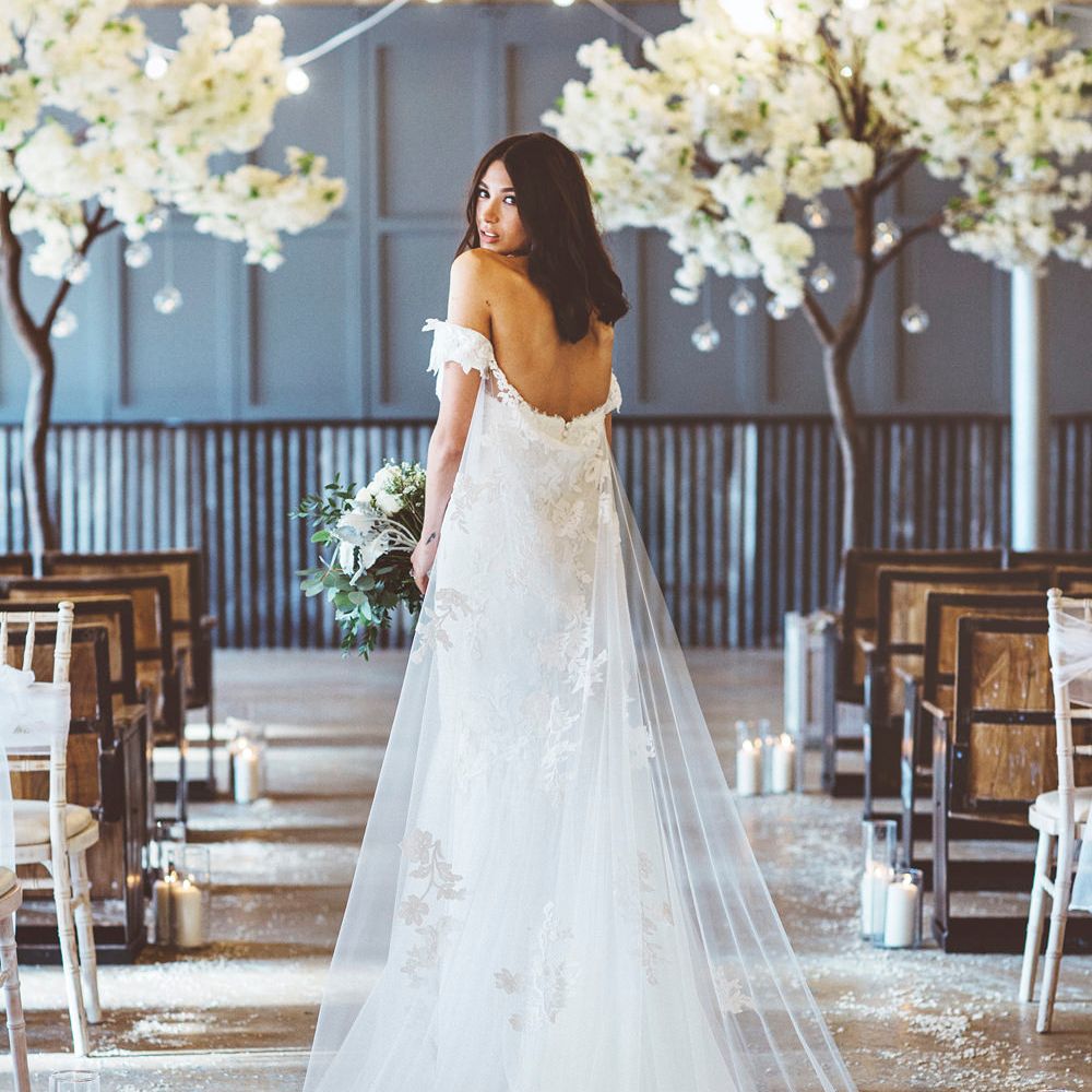 Bride in Embroidered Pronovias Wedding Dress with Off Shoulder Sleeves and Veil Cape | Bride Wearing Hair Down | Bridal Bouquet of White Roses and Greenery | Cherry Blossom Tree Altar | Festoon Lights | Pillar Candles | Aisle Petals | Lace Bridal Cape Veil &amp; Fishtail Wedding Dress by Pronovias | On Love and Photography