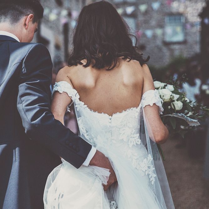 Bride in Fishtail Pronovias Wedding Dress with Off Shoulder Sleeves and Veil Cape | Groom in Navy Tails and Grey Waistcoat | Bride Wearing Hair Down | Bridal Bouquet of White Roses and Greenery | Wedding Bunting | Lace Bridal Cape Veil &amp; Fishtail Wedding Dress by Pronovias | On Love and Photography