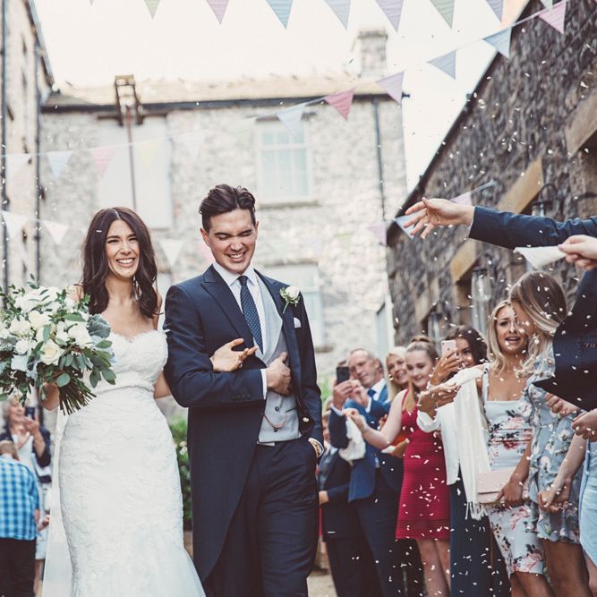 Confetti Throw | Bride in Embroidered Pronovias Wedding Dress with Off Shoulder Sleeves and Veil Cape | Groom in Navy Tails and Grey Waistcoat | Bride Wearing Hair Down | Bridal Bouquet of White Roses and Greenery | Wedding Bunting | Lace Bridal Cape Veil &amp; Fishtail Wedding Dress by Pronovias | On Love and Photography