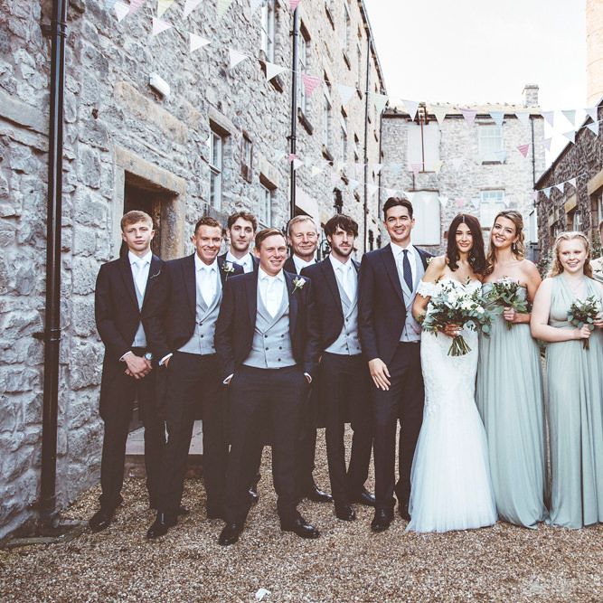 Bride in Fishtail Pronovias Wedding Dress with Off Shoulder Sleeves and Veil Cape | Bride Wearing Hair Down | Bridal Bouquet of White Roses and Greenery | Bridesmaids in Fossil Green Multiway Dresses | Bridesmaid Bouquets of Dusky Purple Roses and Greenery | Groom and Groomsmen in Navy Tails and Grey Waistcoats | Wedding Bunting | Lace Bridal Cape Veil &amp; Fishtail Wedding Dress by Pronovias | On Love and Photography