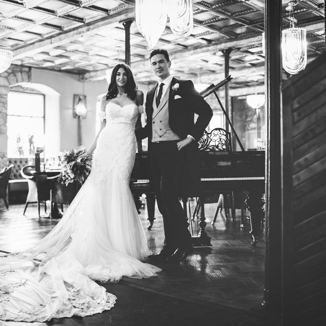 Bride in Fishtail Pronovias Wedding Dress with Off Shoulder Sleeves and Veil Cape | Groom in Navy Tails and Grey Waistcoat | Bride Wearing Hair Down | Bridal Bouquet of White Roses and Greenery | Lace Bridal Cape Veil &amp; Fishtail Wedding Dress by Pronovias | On Love and Photography