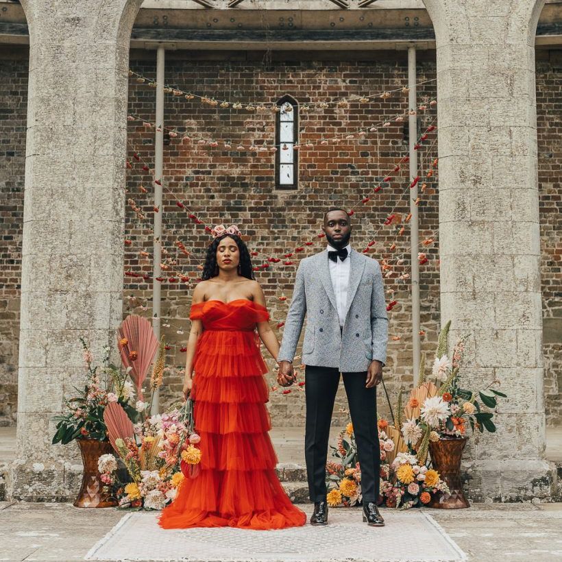 Stylish bride and groom in red dress and grey blazer at Chiddingstone Castle