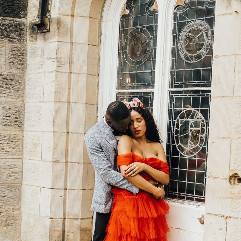 Groom in grey blazer embracing his bride in a strapless red wedding dress