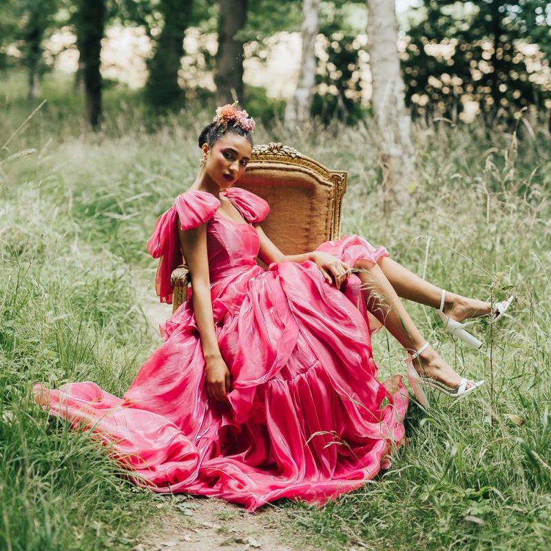 bride in pink wedding dress sitting on a chair in the woods at Chiddingstone Castle