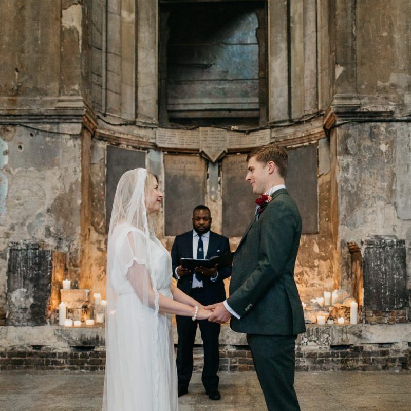 Bride wearing a sophisticated dress with lace tipped veil with her groom at London wedding  with candle light backdrop